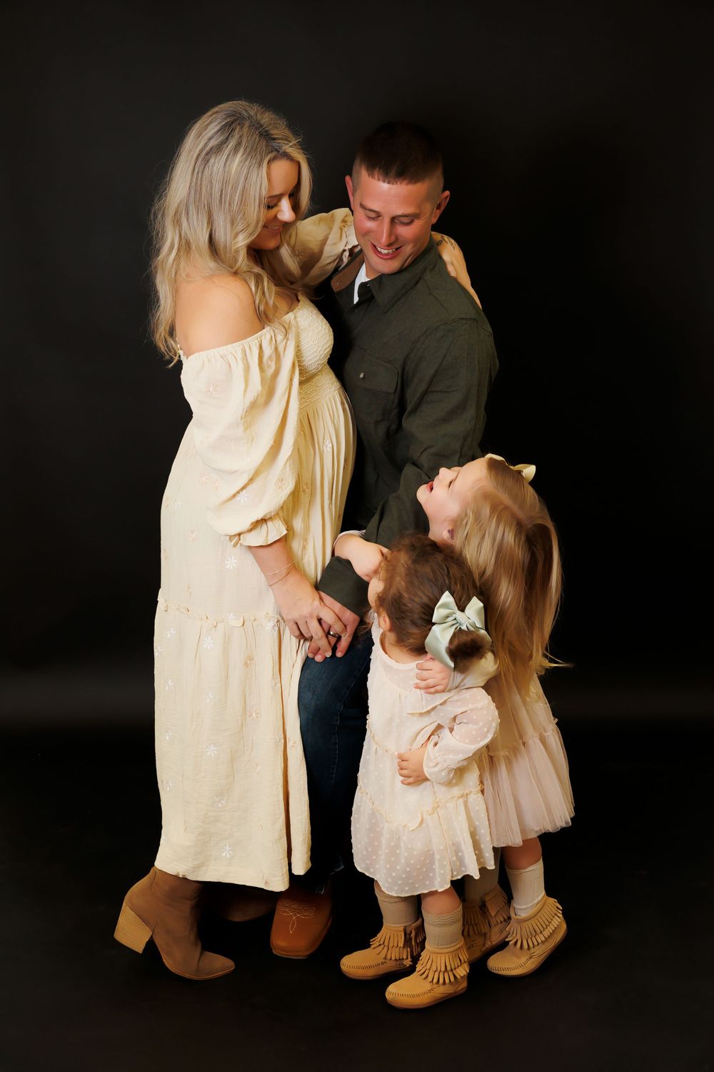 A family portrait against a dark background showing tender interactions and coordinated cream-colored outfits.