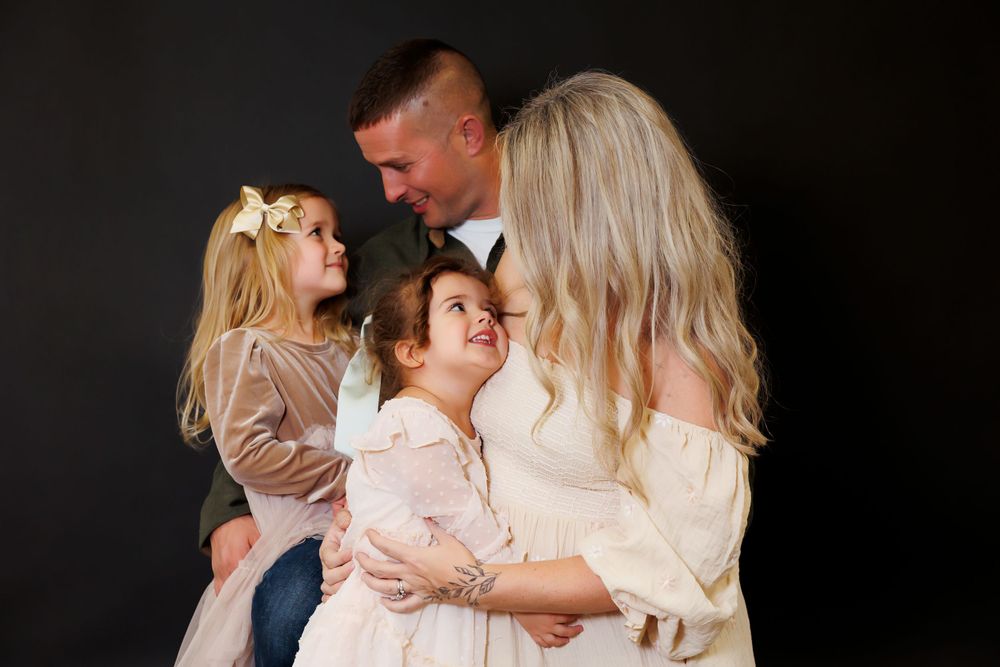 An emotional family portrait against black background with everyone dressed in light colored clothing.