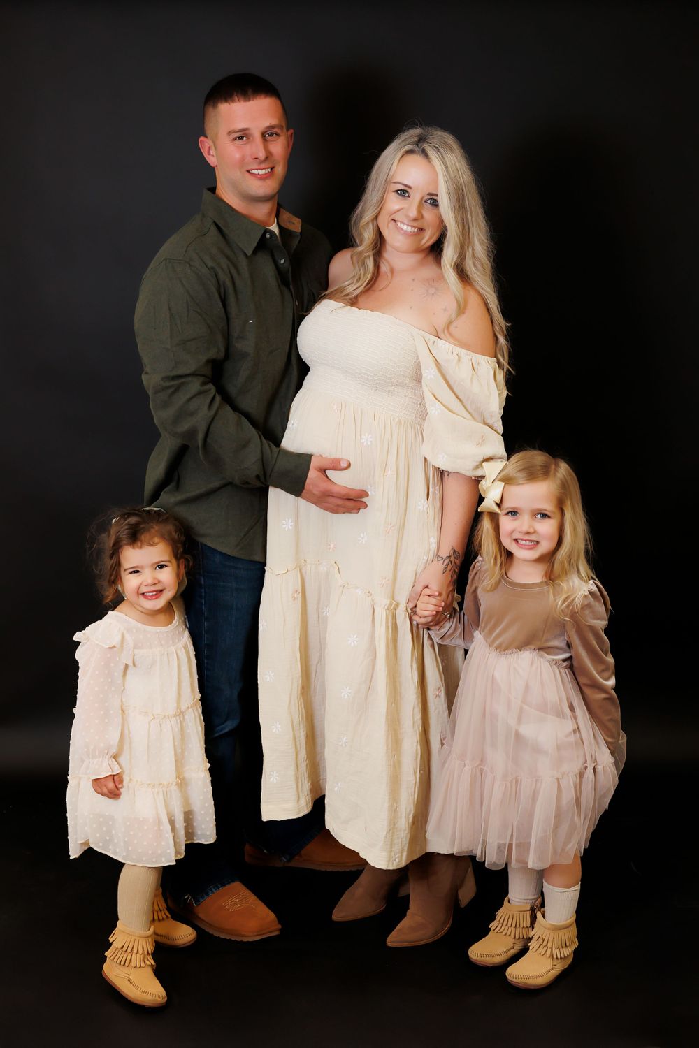 A family maternity portrait features parents and two young children in coordinating cream and neutral outfits.