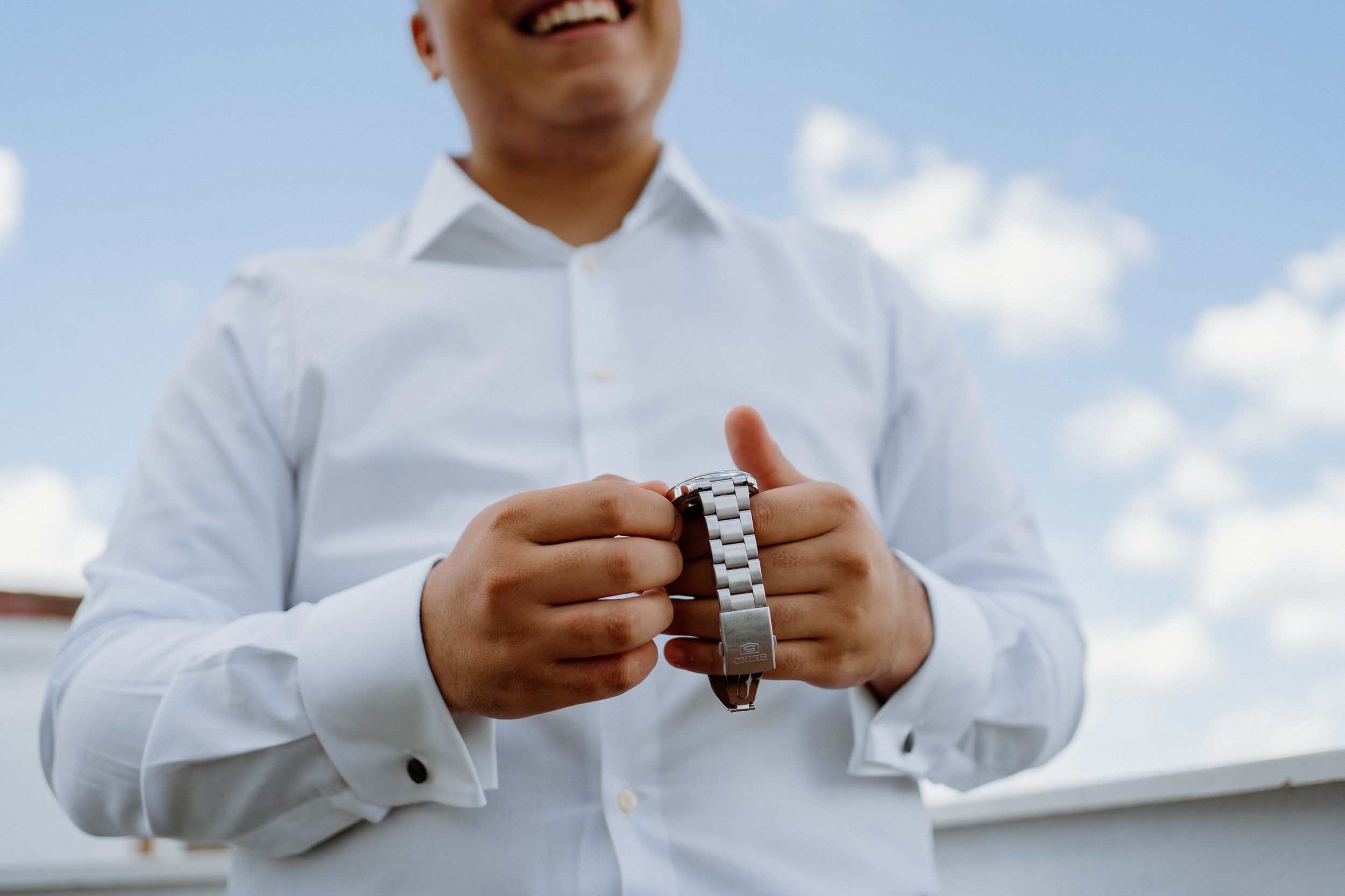 Someone in a white dress shirt holding a leather bracelet or wristband against a bright blue sky background.