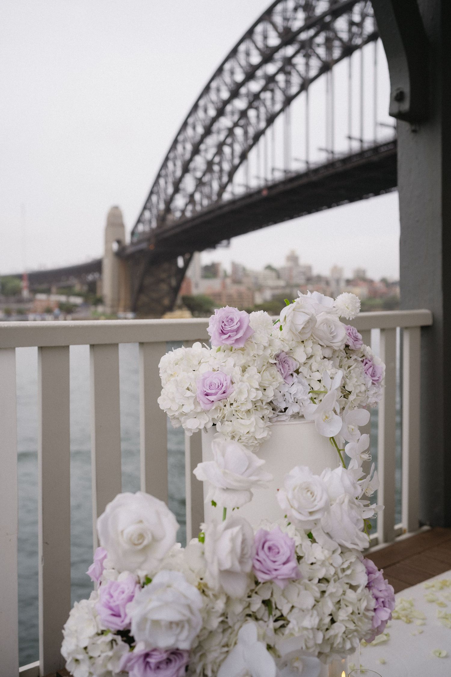 White and purple floral arrangements with a bridge backdrop over water.