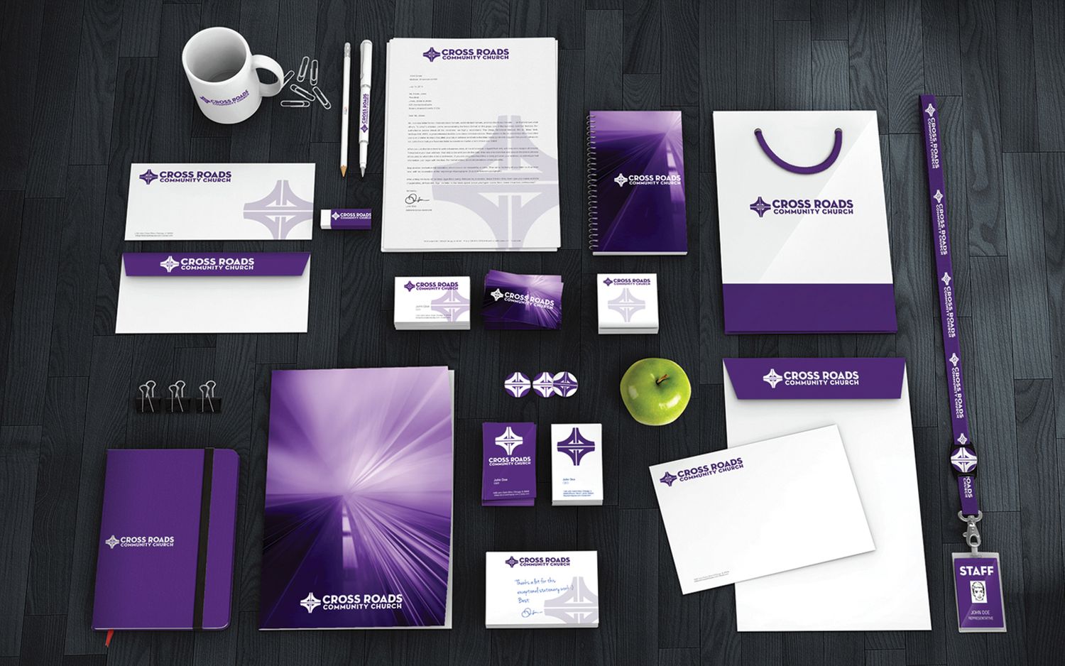 A business branding mockup featuring purple and white stationery items, cards, and folders laid out on a dark surface.