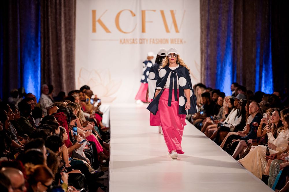 Fashion show runway with illuminated catwalk and audience seating visible.