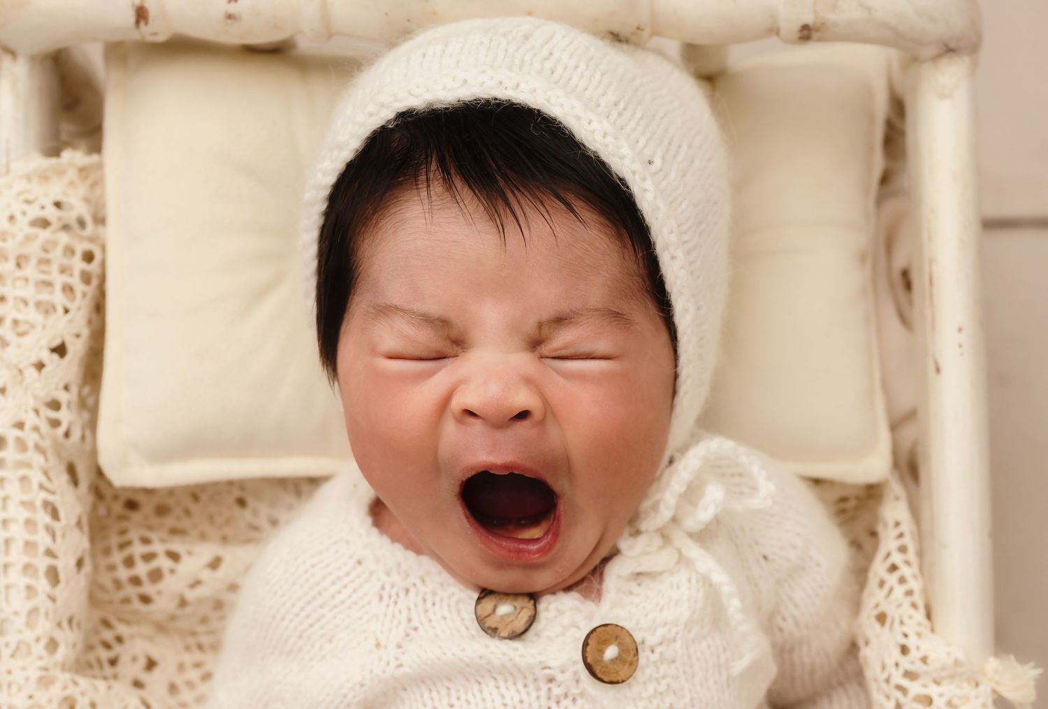 Baby girl with thick brown hair and a soft white hat and romper yawning in Charlottesville, Virginia.