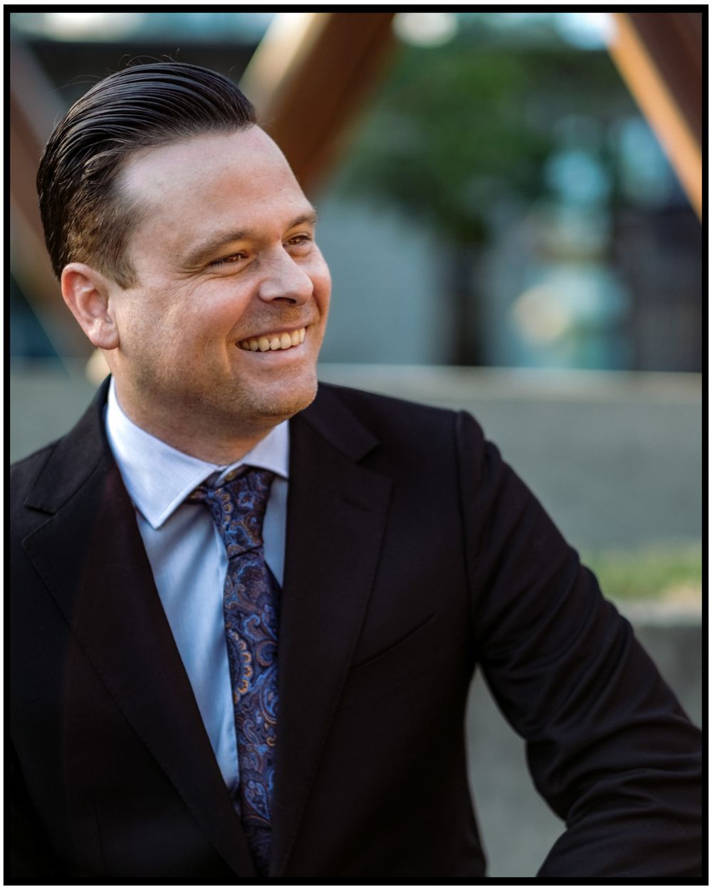 Professional headshot of a businessman in a dark suit and patterned tie with a warm smile.