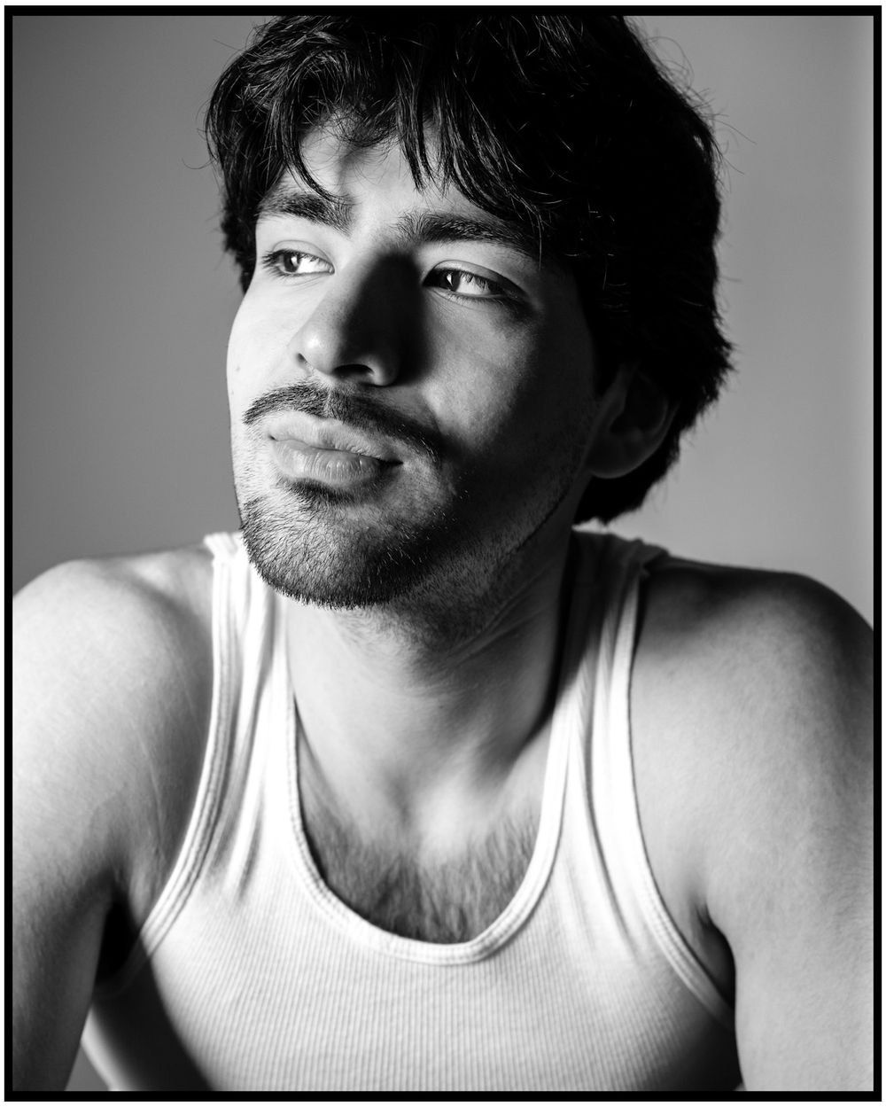 Black and white portrait of a person wearing a white tank top in dramatic studio lighting.