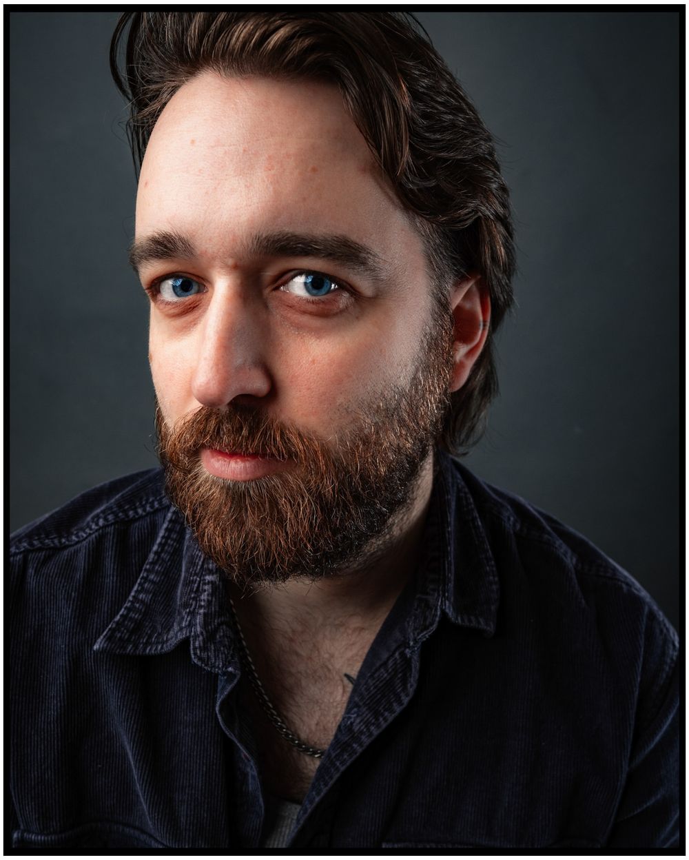 Dramatic portrait of person with beard wearing dark shirt against moody background.