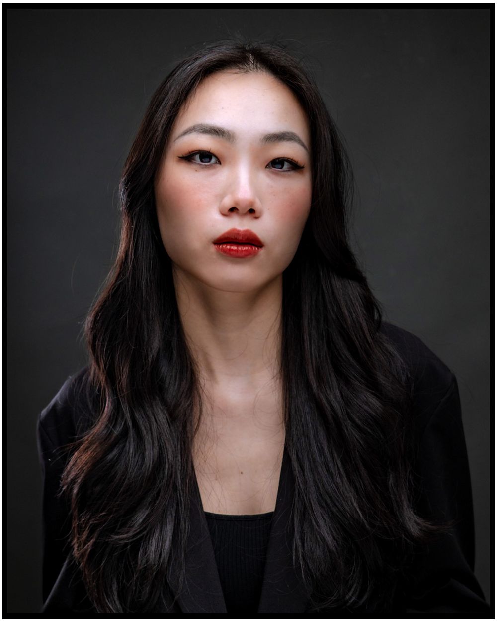 Dramatic portrait against dark background shows long black hair and red lipstick with minimalist black attire.