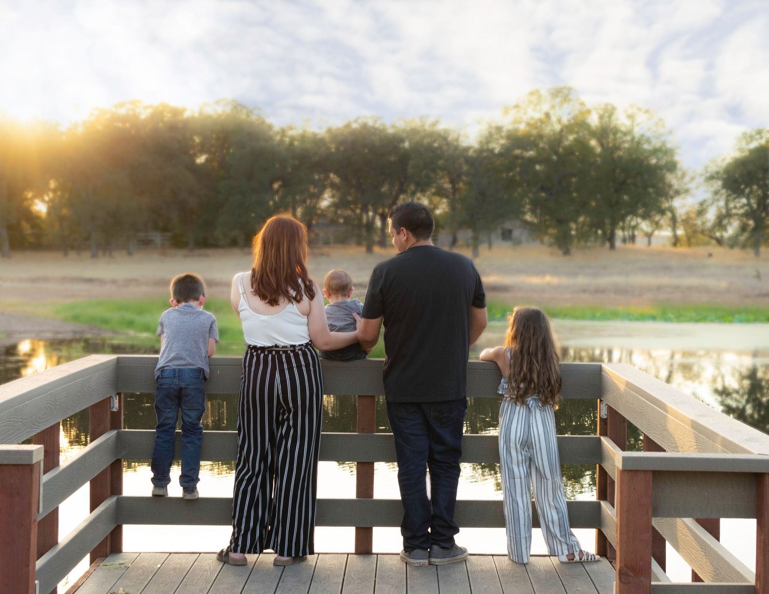 Family standing together on wooden dock at sunset overlooking water.