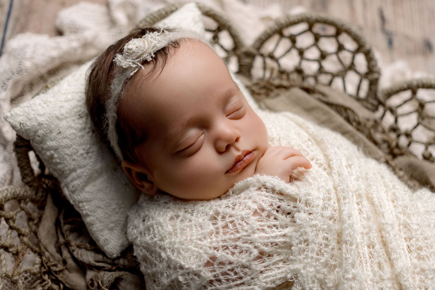A sleeping baby wrapped in delicate white lace swaddle rests peacefully on a textured blanket.