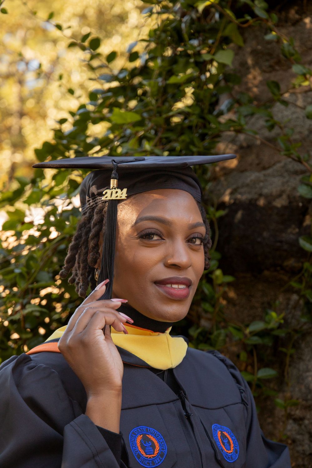 Graduate in academic regalia with tasseled cap smiling outdoors in autumn setting.