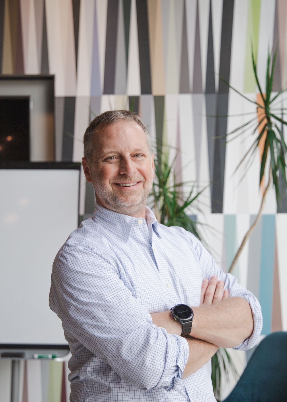 Professional portrait of figure in white button-up shirt smiling against modern office backdrop.