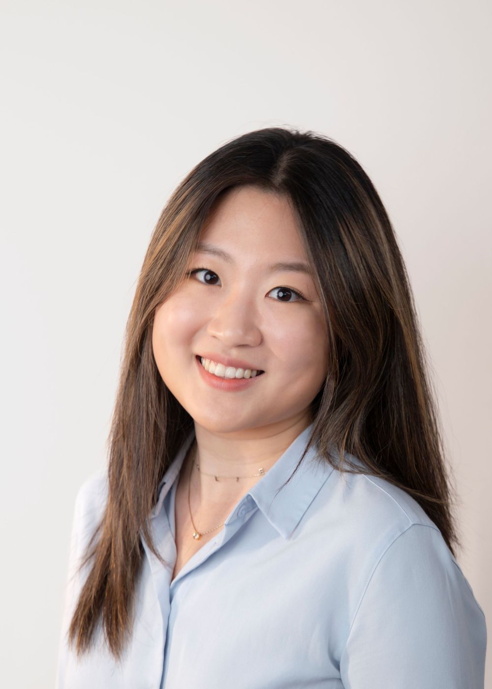 Professional headshot of woman in light blue button-down shirt against white background.