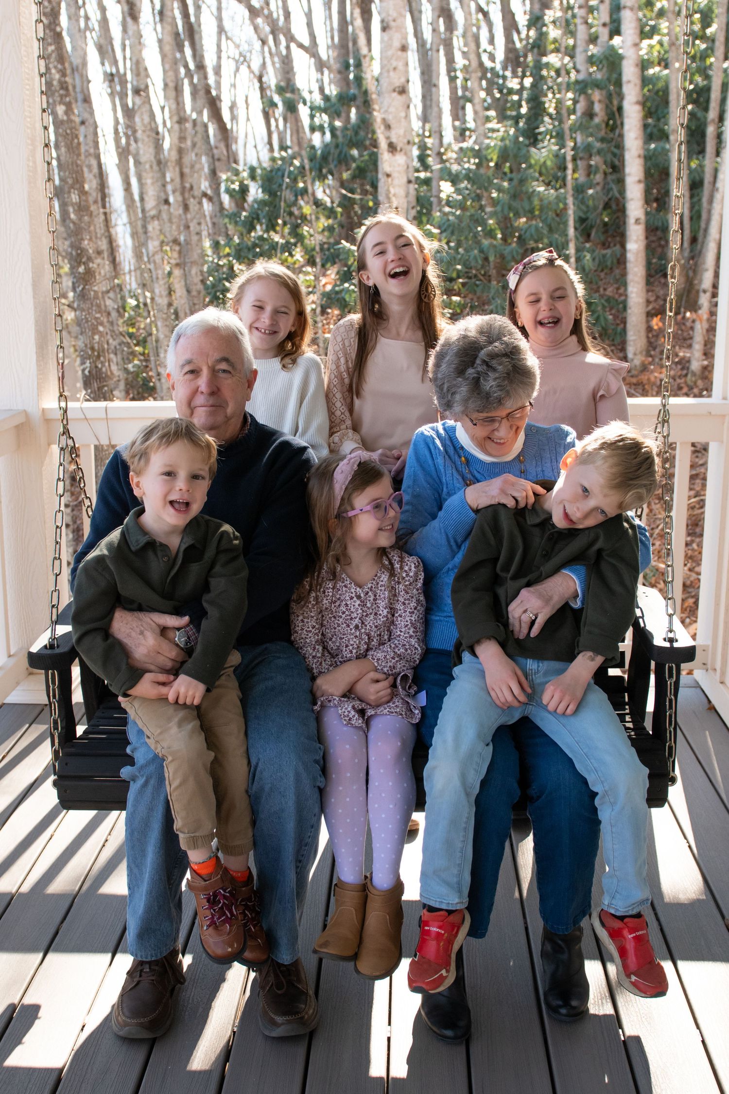 A group of people sitting together on a wooden porch bench in sunlight, creating a candid outdoor family moment.