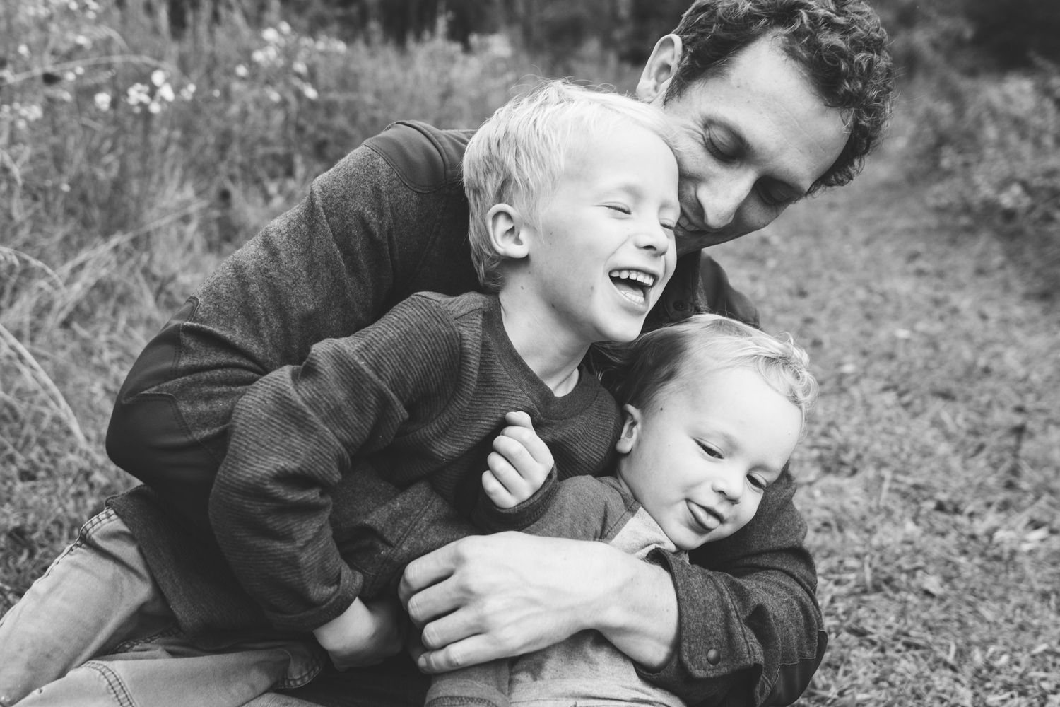 Black and white photo showing joyful moment between parent and children playing outdoors in nature.