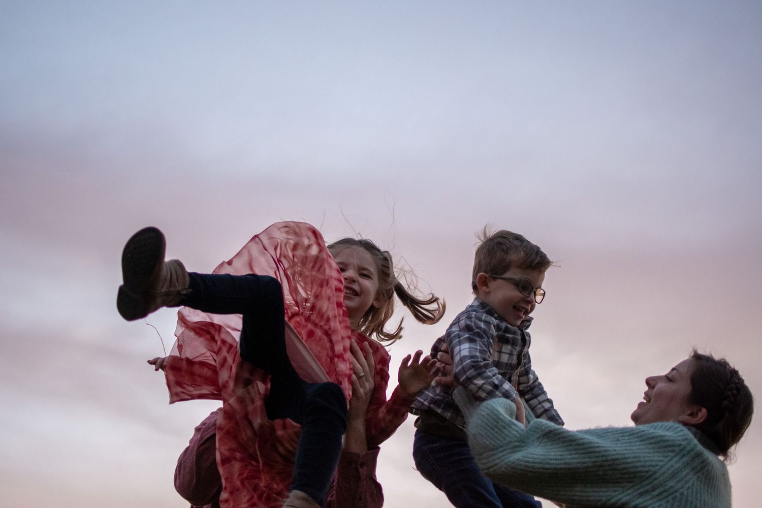 Playful family moment captured during sunset as figures leap and play together in silhouette.
