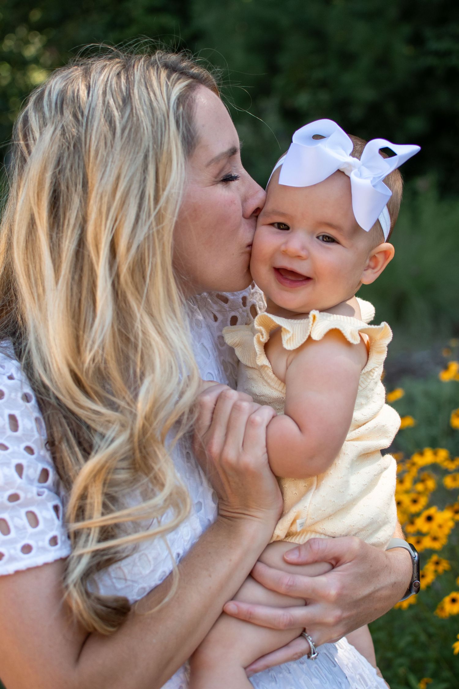 Mother and baby share tender moments in a garden with yellow flowers during a summer photoshoot.