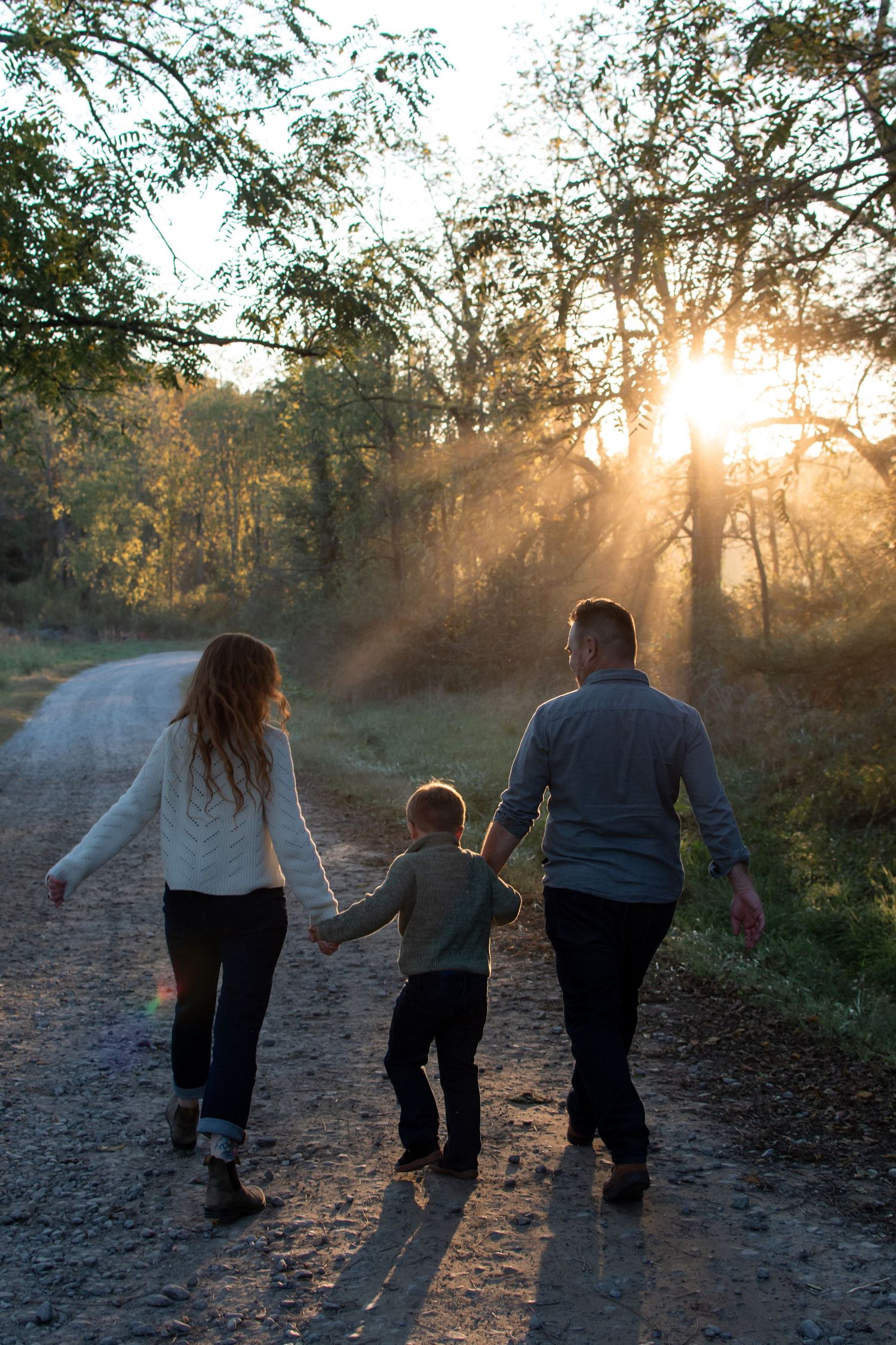 Family walks together on a dirt path at sunset with golden sunlight streaming through autumn trees.