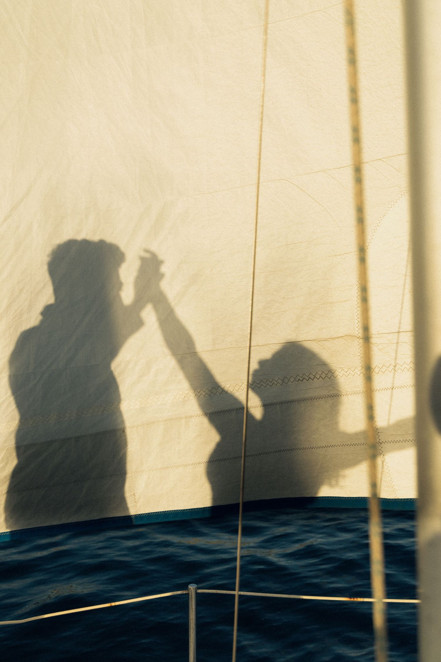 Shadow silhouettes cast on a sail against golden sky with ocean waves visible below on a sailing boat.