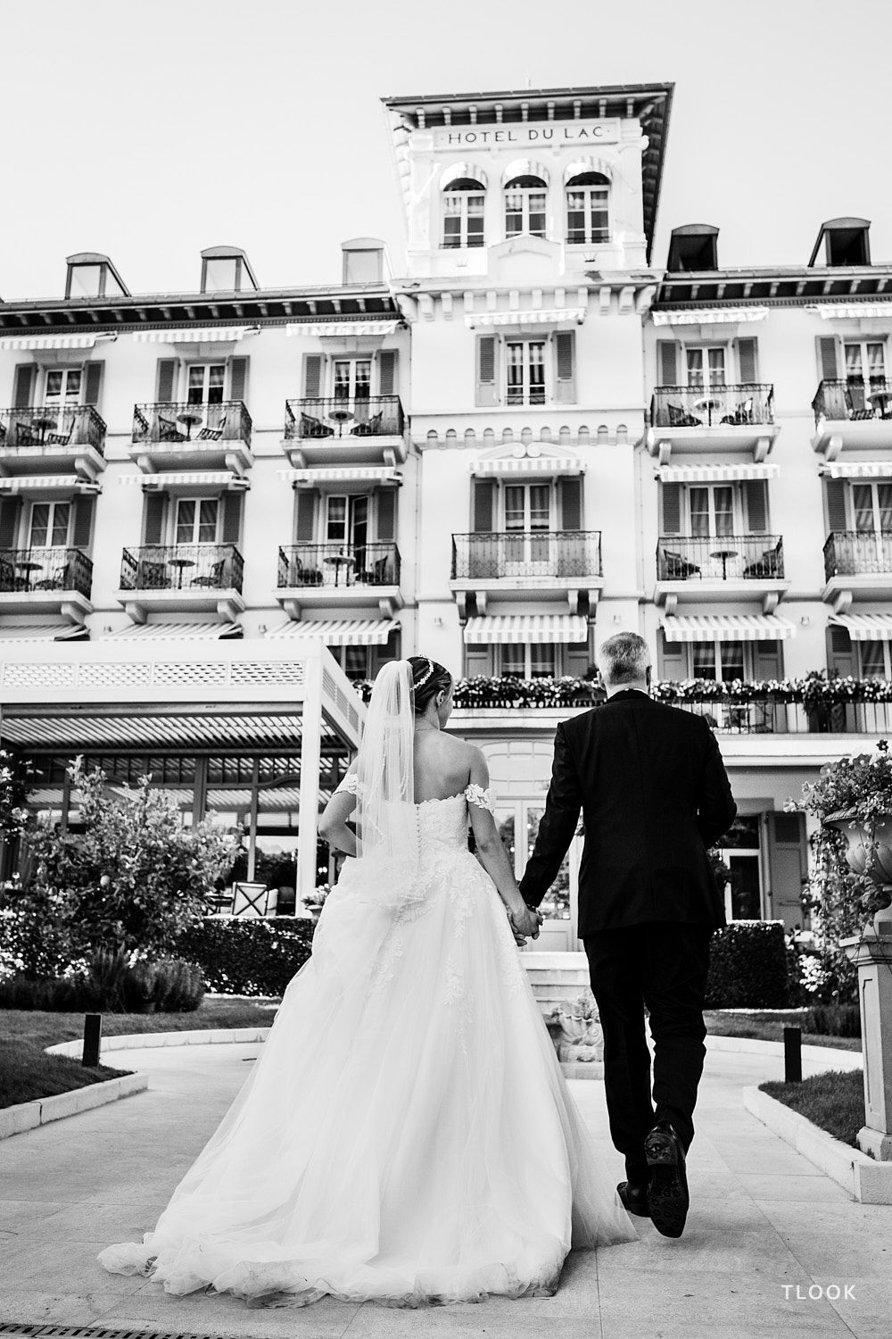 TLOOK photographe de mariage de style documentaire, portrait des mariés qui arrivent au grand hôtel du lac en se tenant par la main