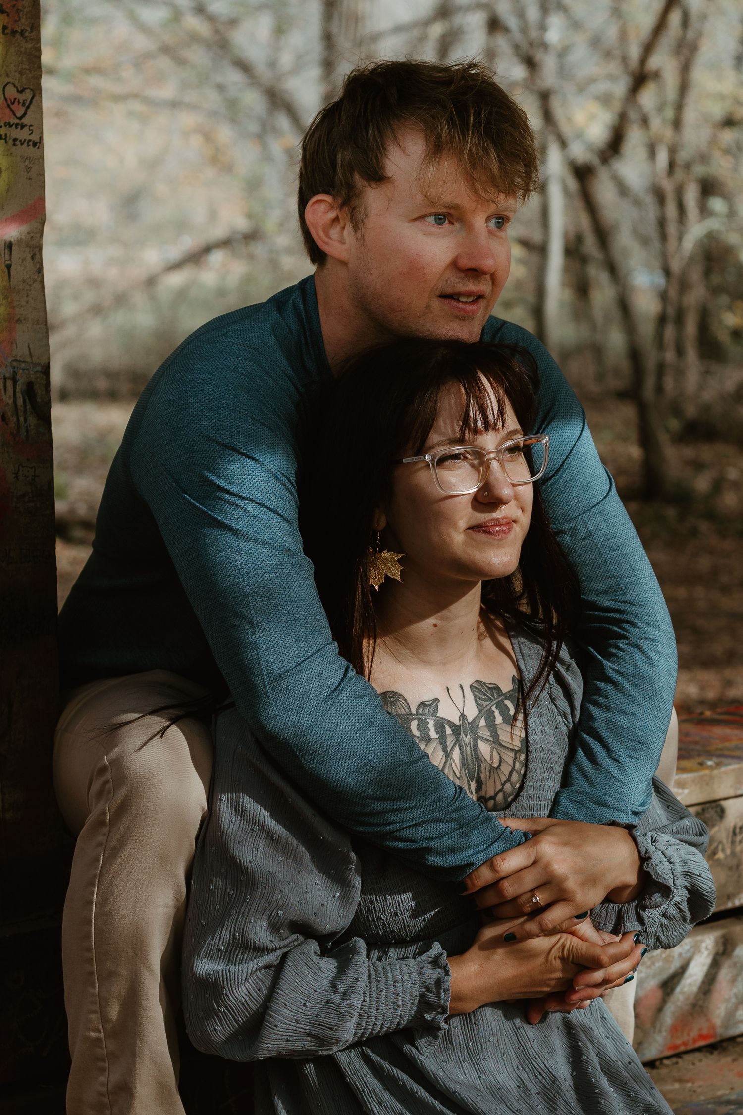 A romantic autumn portrait of a couple embracing outdoors with soft natural lighting and fall foliage in the background.