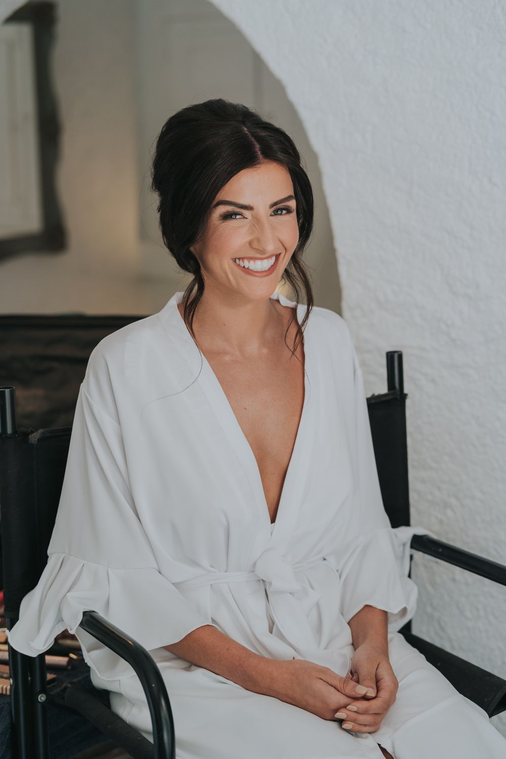 A woman in a white robe smiles while seated in preparation for a special event.