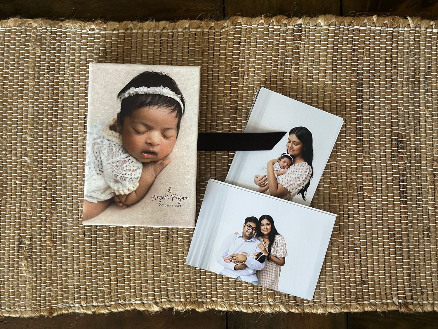 Professional photographs laid out on a textured beige surface showing maternity and newborn portraits.
