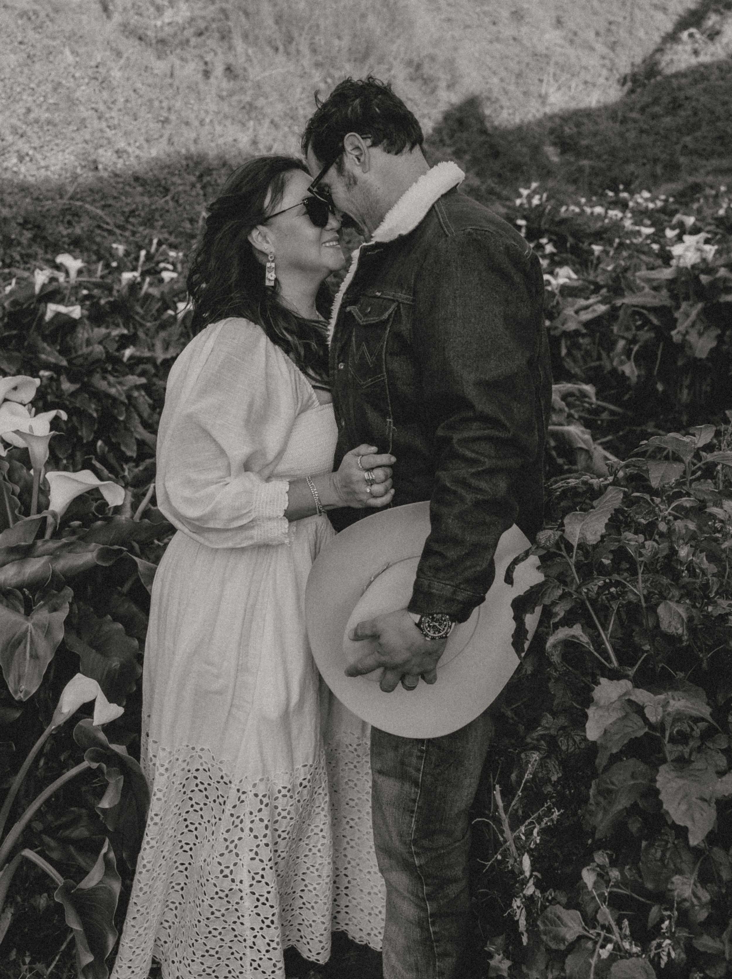 A romantic black and white photograph shows a tender moment between two people embracing in a garden setting.