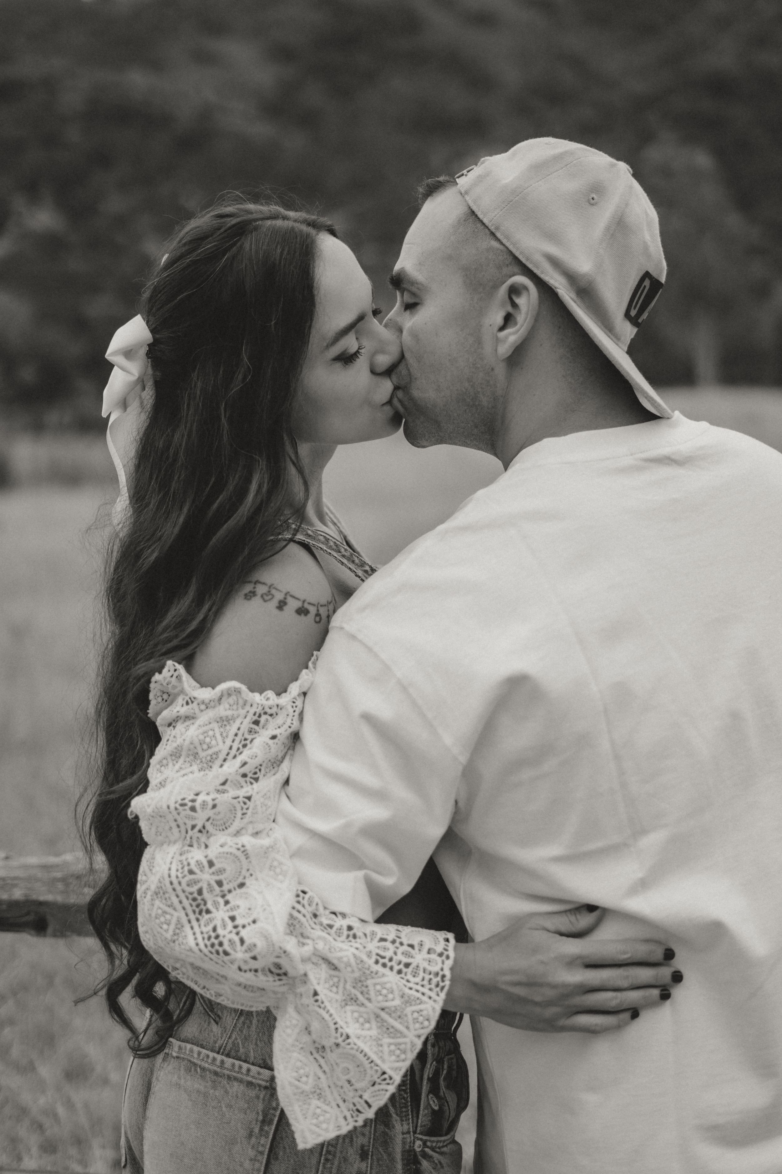A romantic black and white photo shows a couple sharing a tender kiss outdoors, wearing casual attire.