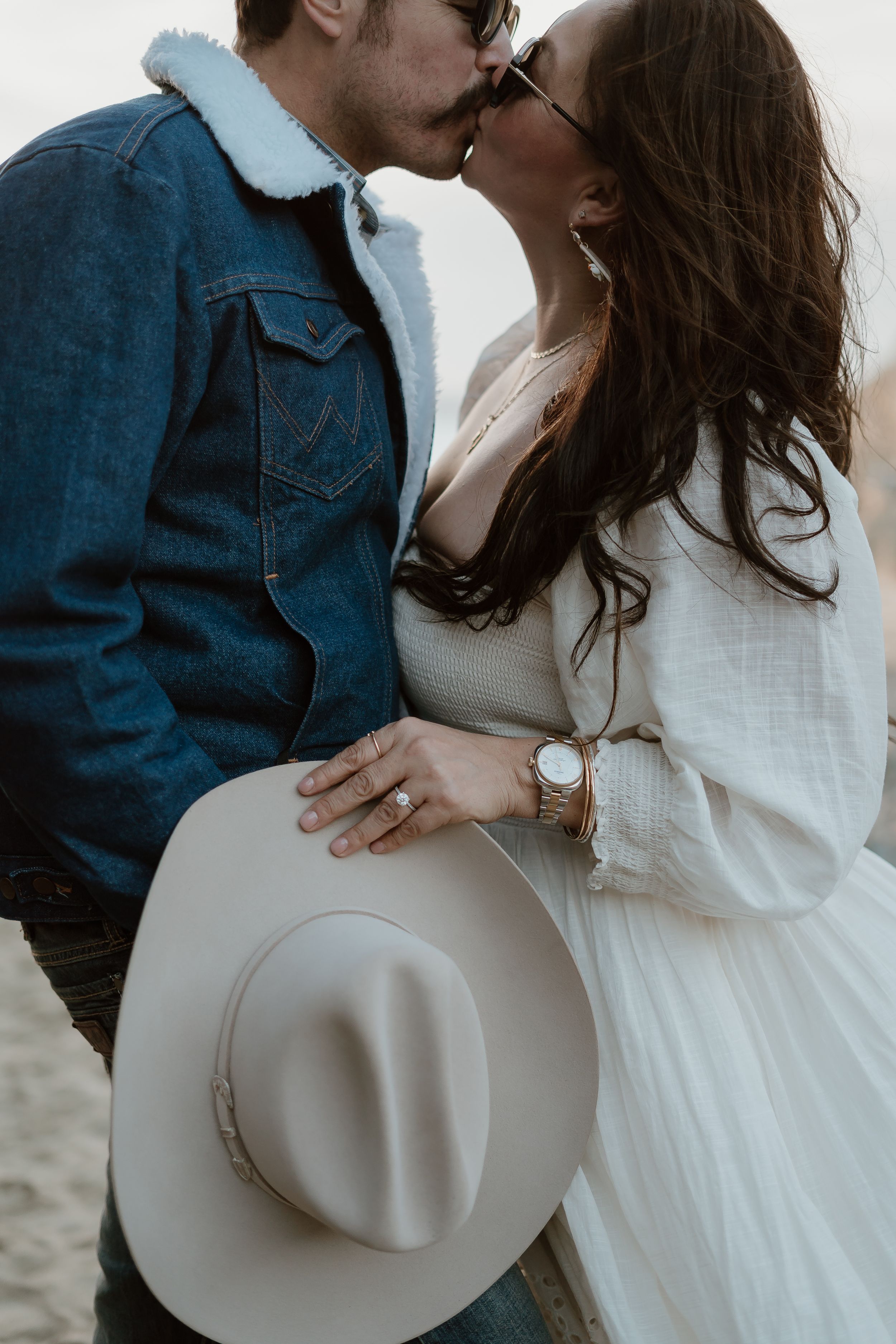 A romantic couple in denim and white sharing an intimate moment while holding a light-colored western hat.