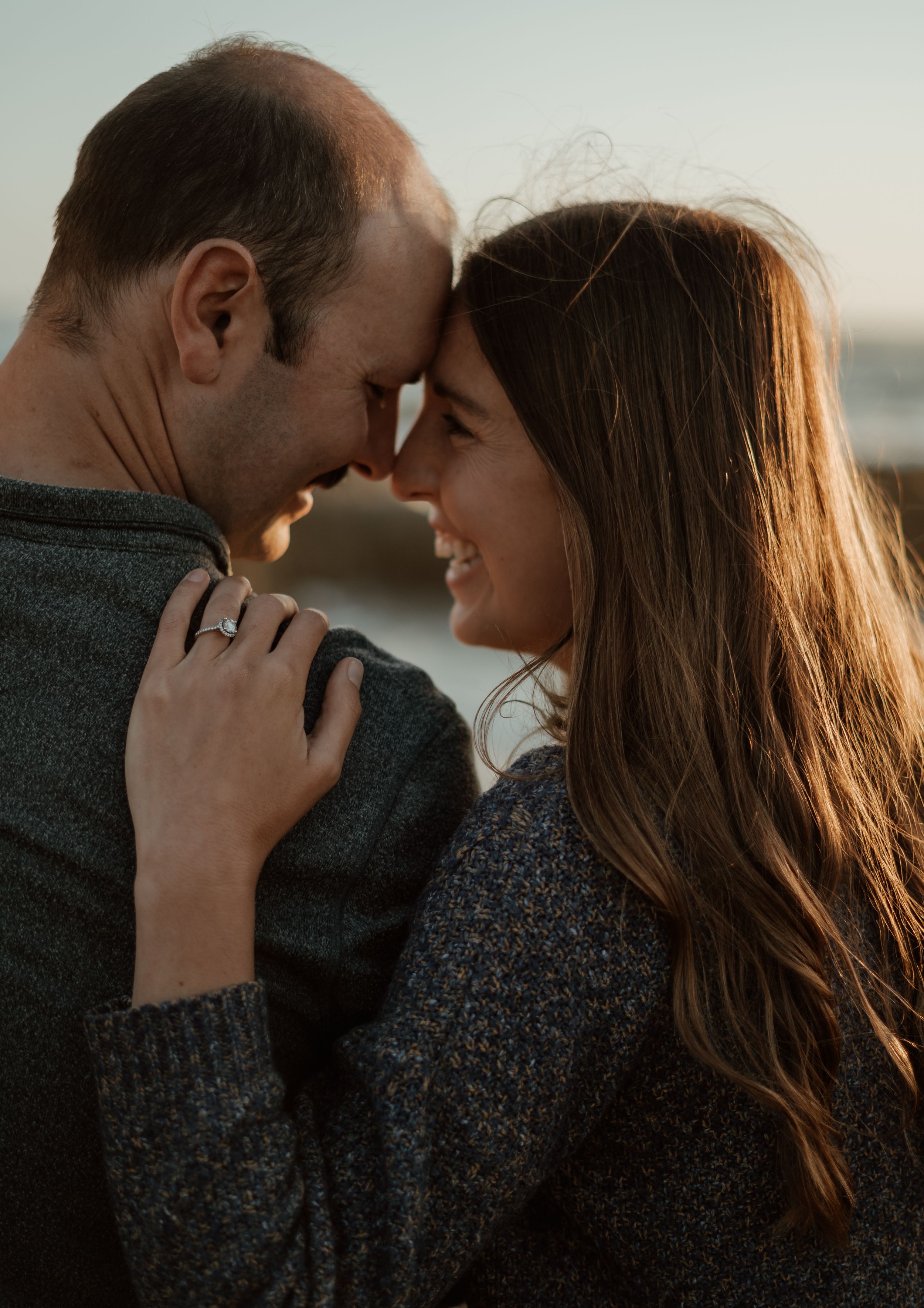 Intimate couple sharing a tender moment outdoors at sunset, both wearing cozy sweaters.
