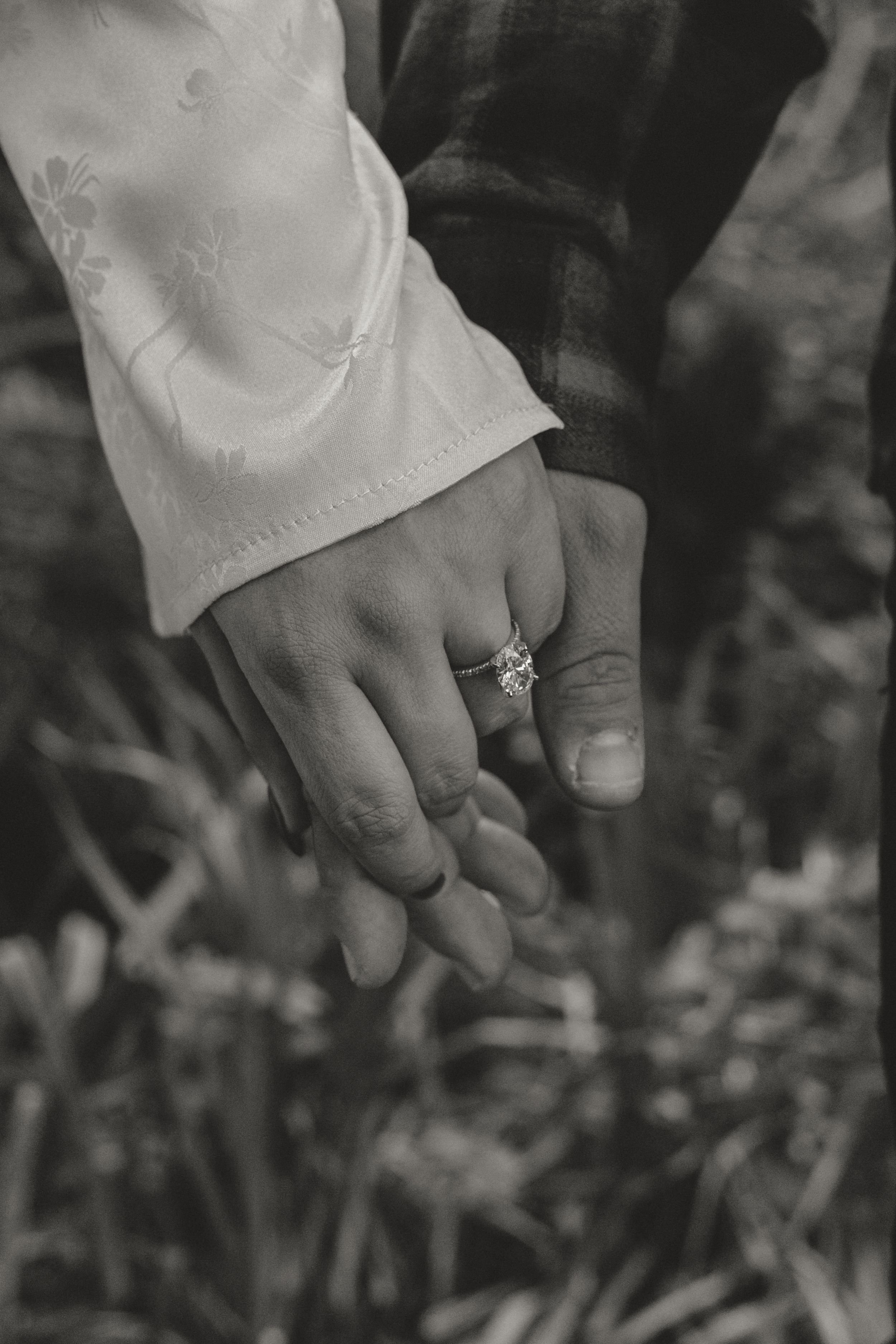Black and white close-up photo of two hands holding each other with an engagement ring visible.