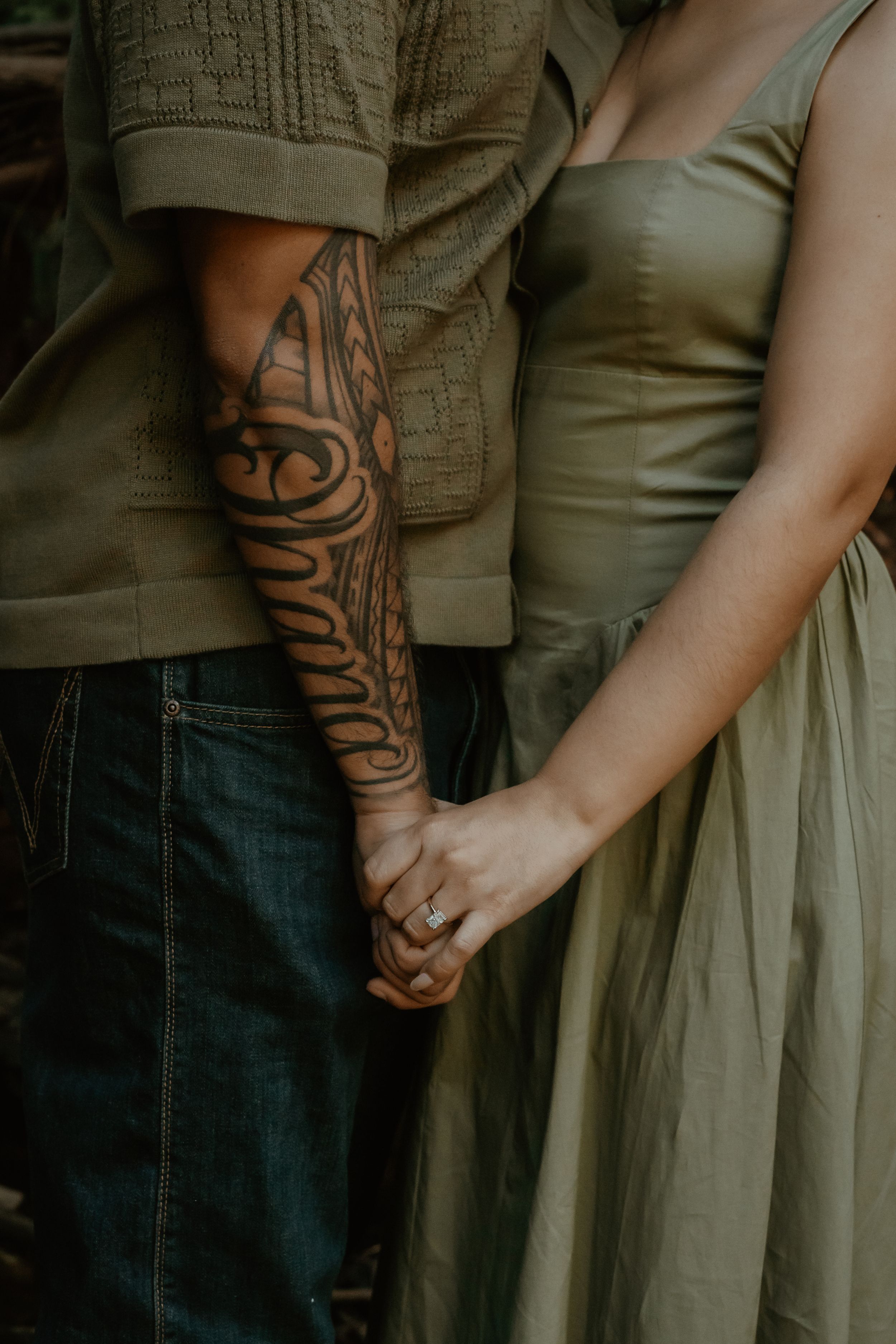 Close-up of a couple holding hands, with one person wearing a tribal tattoo sleeve and olive green clothing.