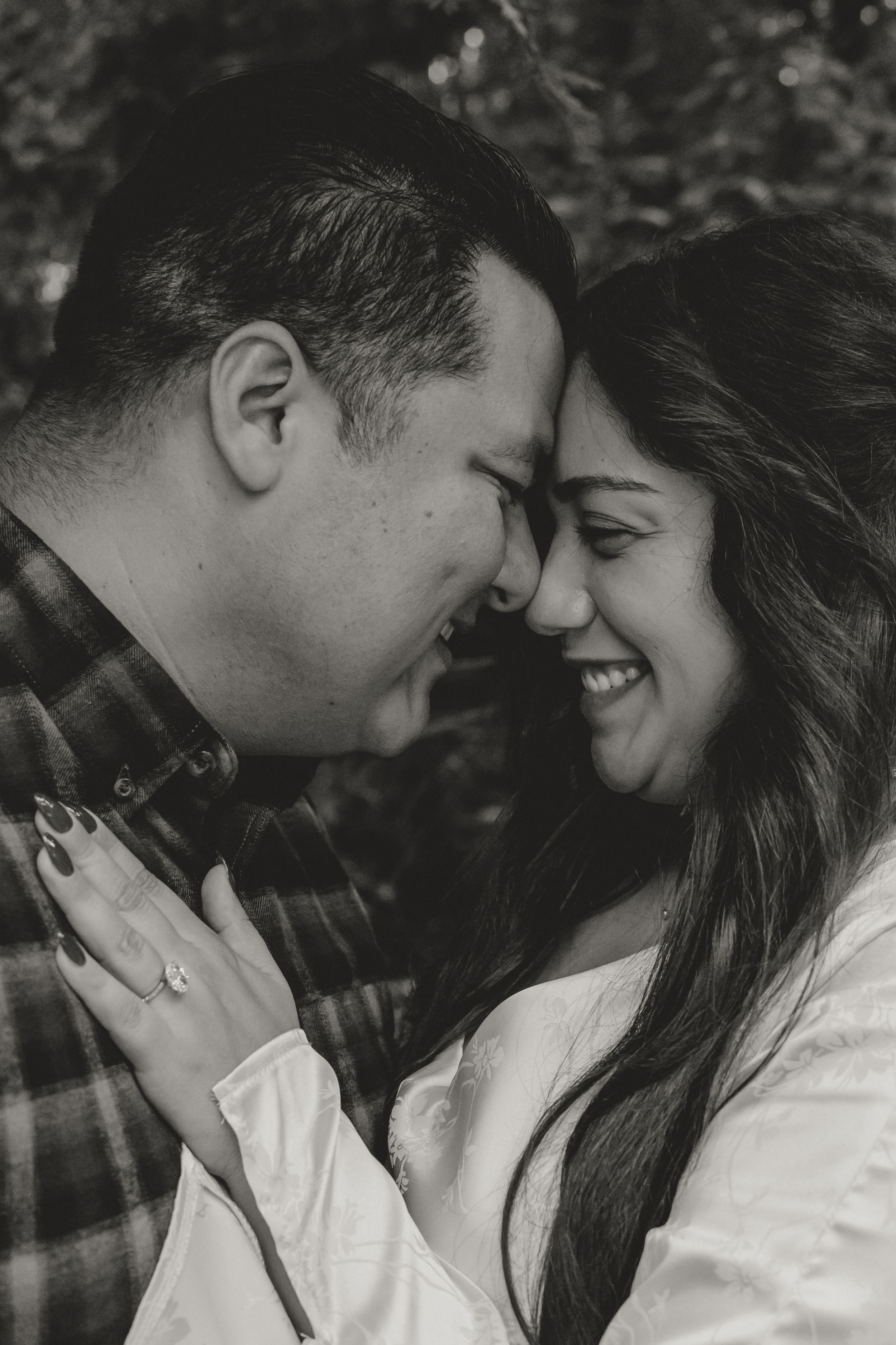 A romantic black and white close-up portrait of a couple sharing an intimate moment with eyes closed and bright smiles.