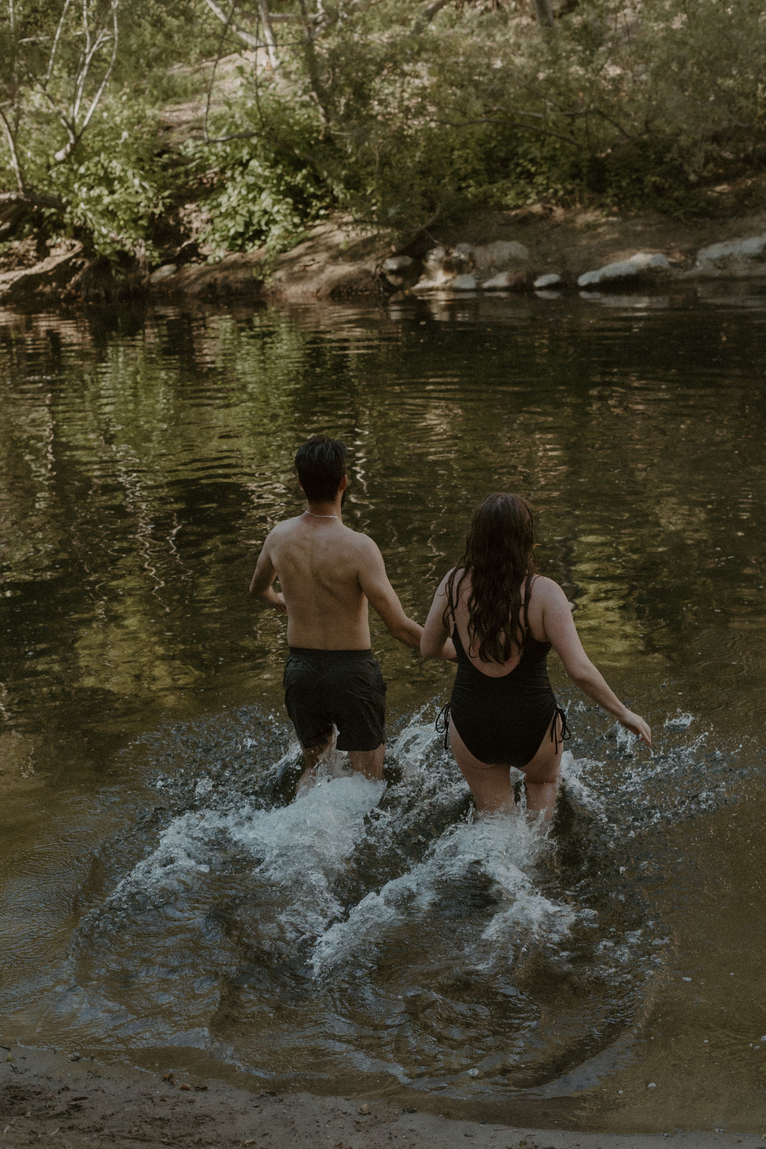 Two people create a joyful splash as they run together into a peaceful woodland stream on a summer afternoon.