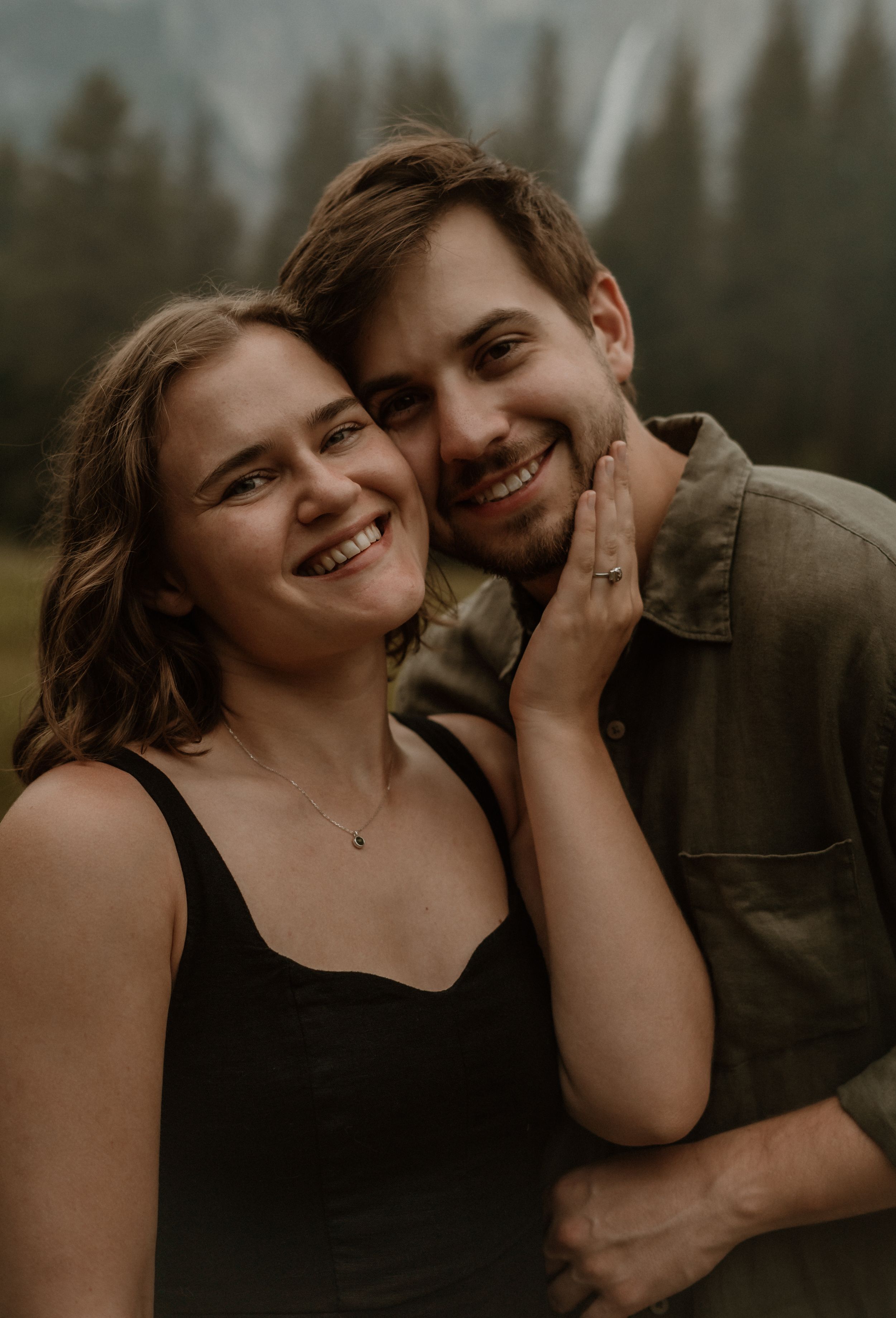 A loving couple shares a tender moment and laughter together in a moody outdoor setting during golden hour.