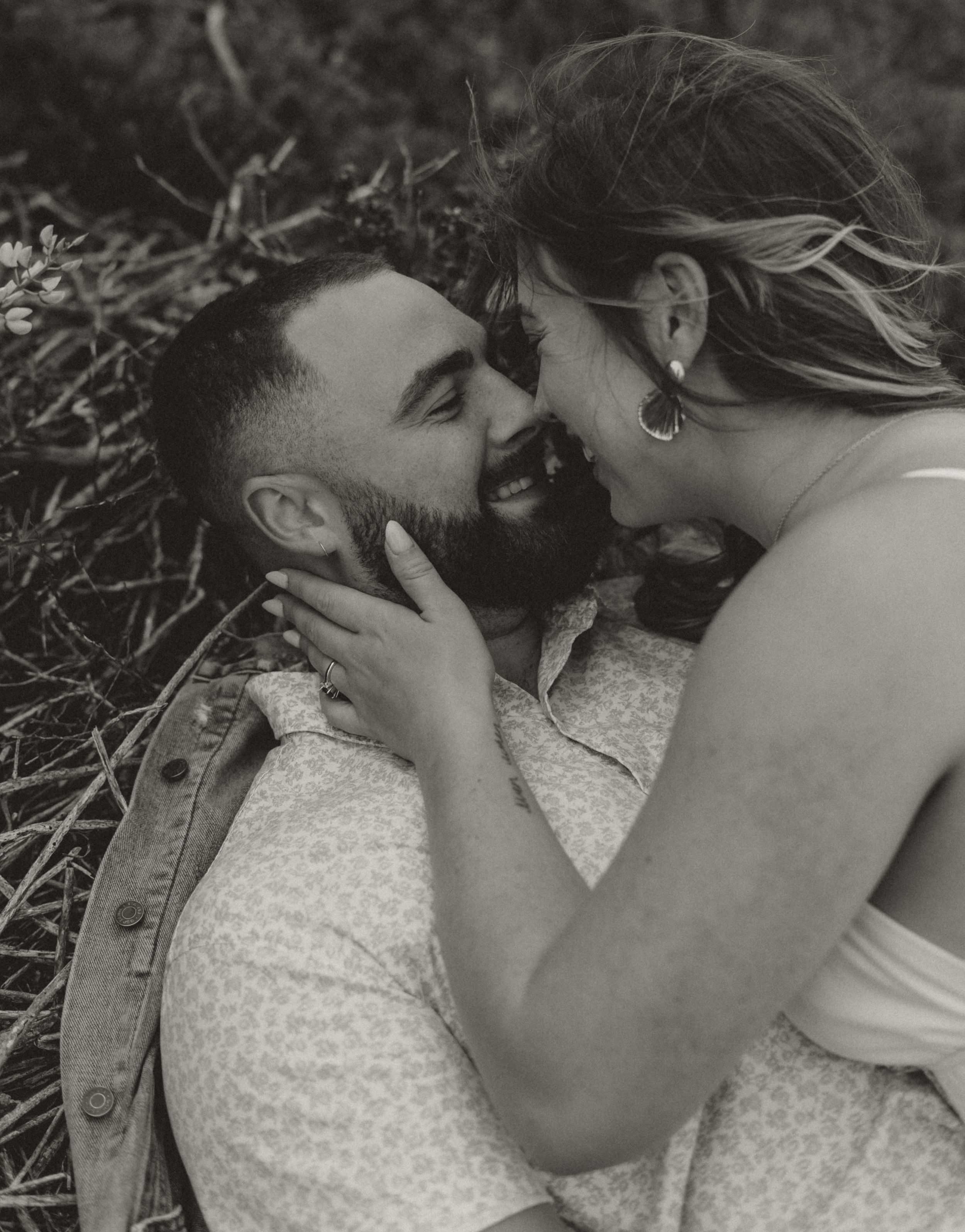 Black and white intimate portrait of a couple lying in grass sharing a tender romantic moment together.