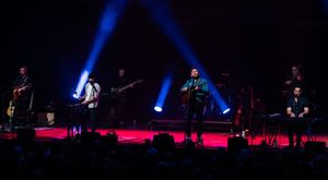 Stage performers silhouetted against dramatic blue lighting during a concert performance.
