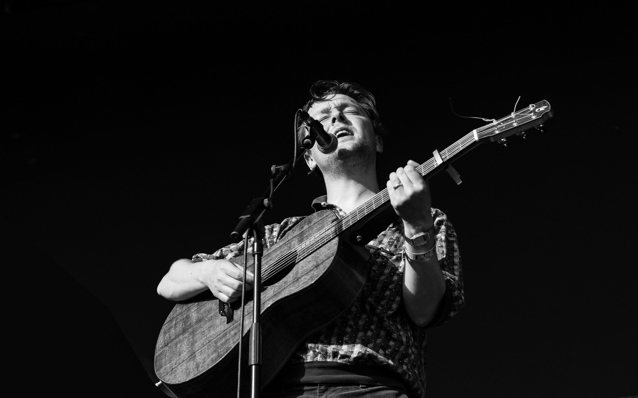 Black and white photo of a smiling musician playing acoustic guitar on stage at a live concert performance.