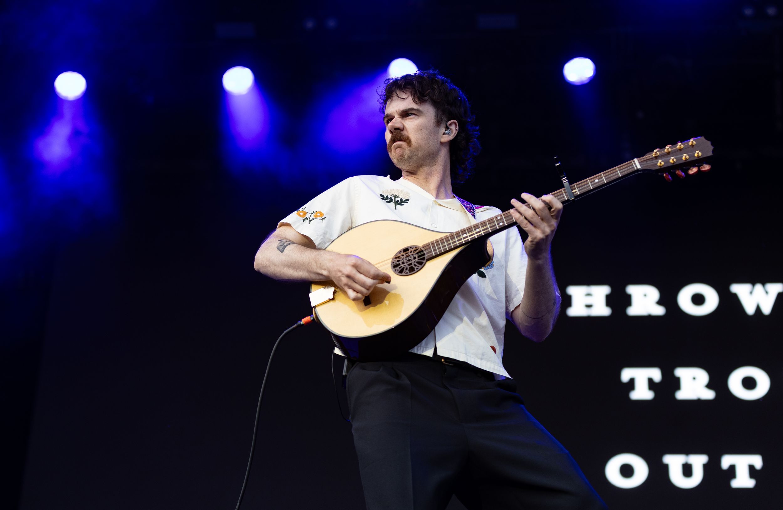 Male musician playing a mandolin on stage under blue lights at a live concert performance.