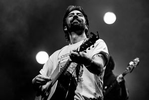 Black and white concert photo of guitarist performing under stage lights.