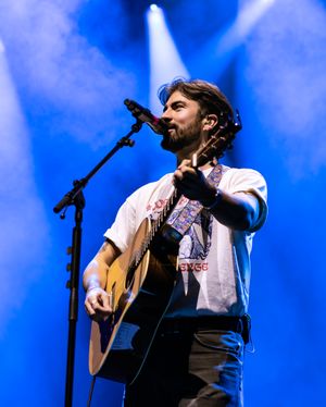 Musician performs on acoustic guitar under dramatic blue stage lighting at live concert.