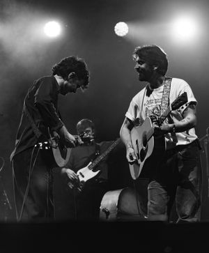 Black and white photo of band members playing guitars together on stage during performance.