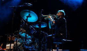 Drummer performs on stage with dramatic blue lighting and concert atmosphere.