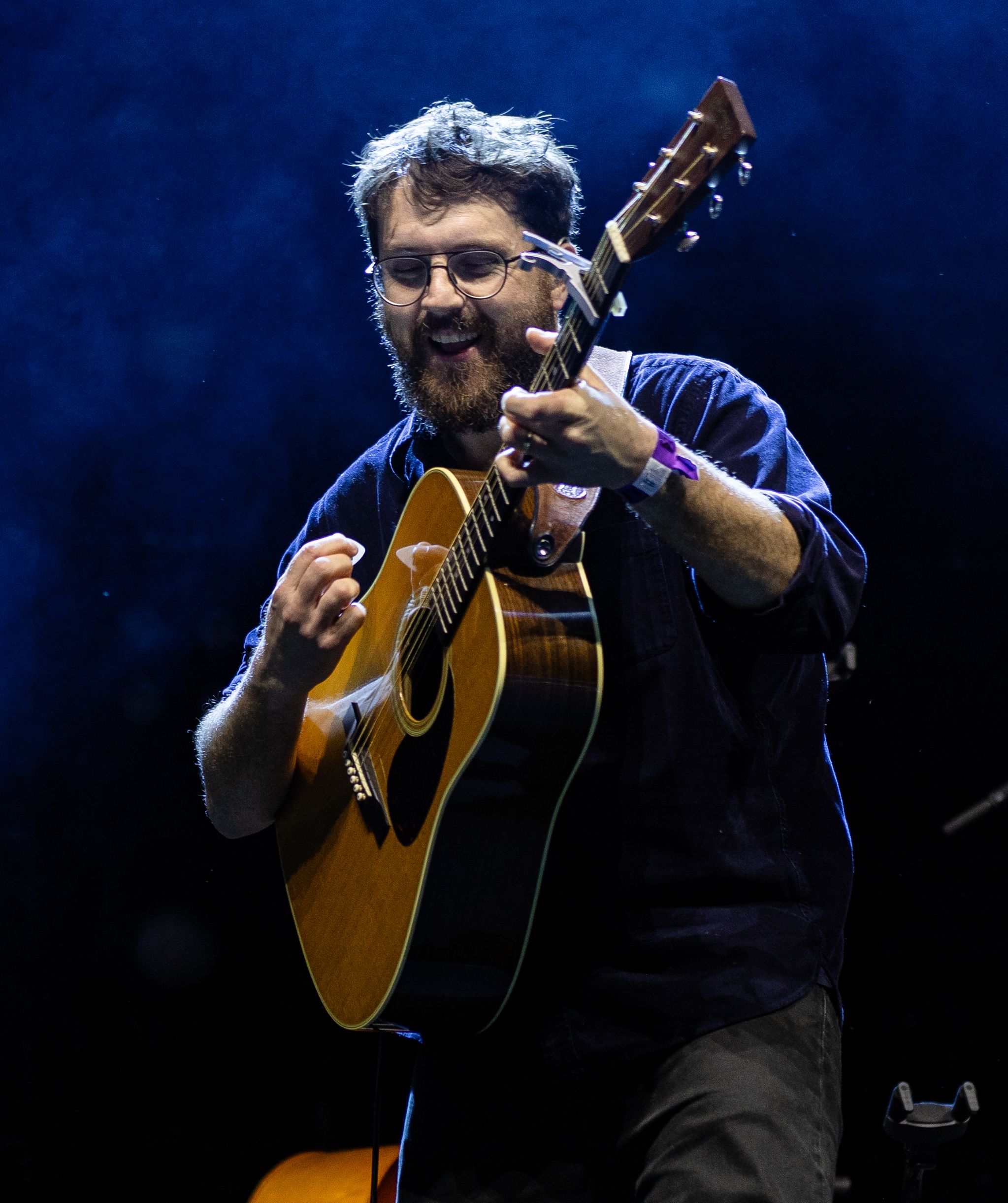 Performer plays acoustic guitar on stage with intense blue lighting.