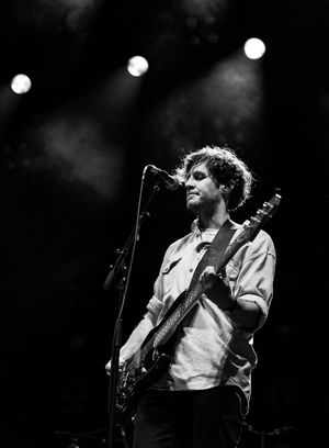 Musician performs with guitar on stage with dramatic spotlight lighting in black and white.
