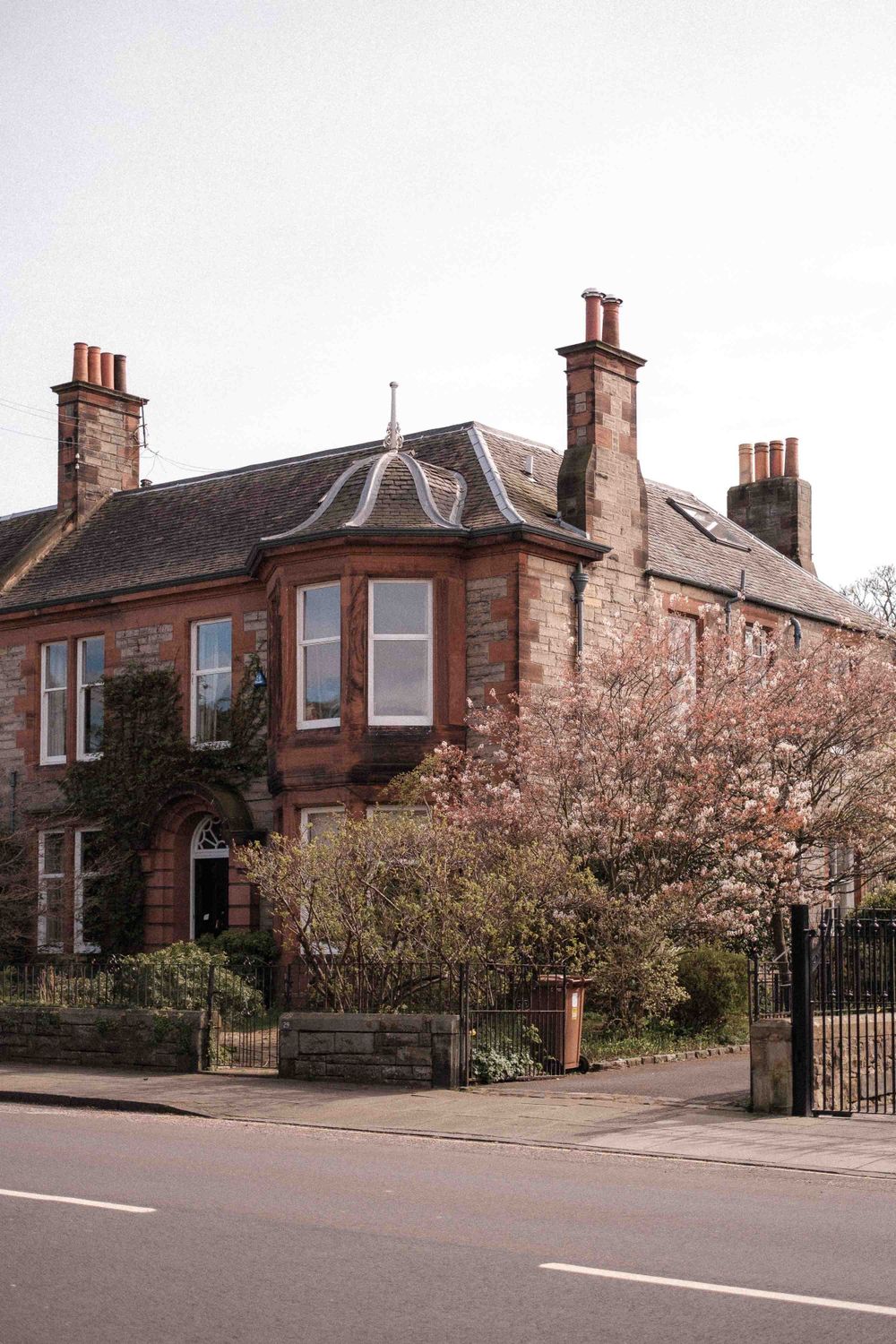 A traditional Scottish sandstone villa with bay windows and multiple chimneys on a residential street.