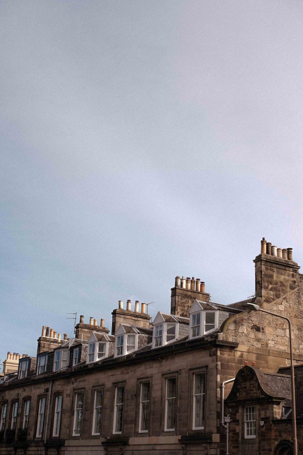 Row of traditional Edinburgh tenement buildings with distinctive chimney pots against cloudy sky.