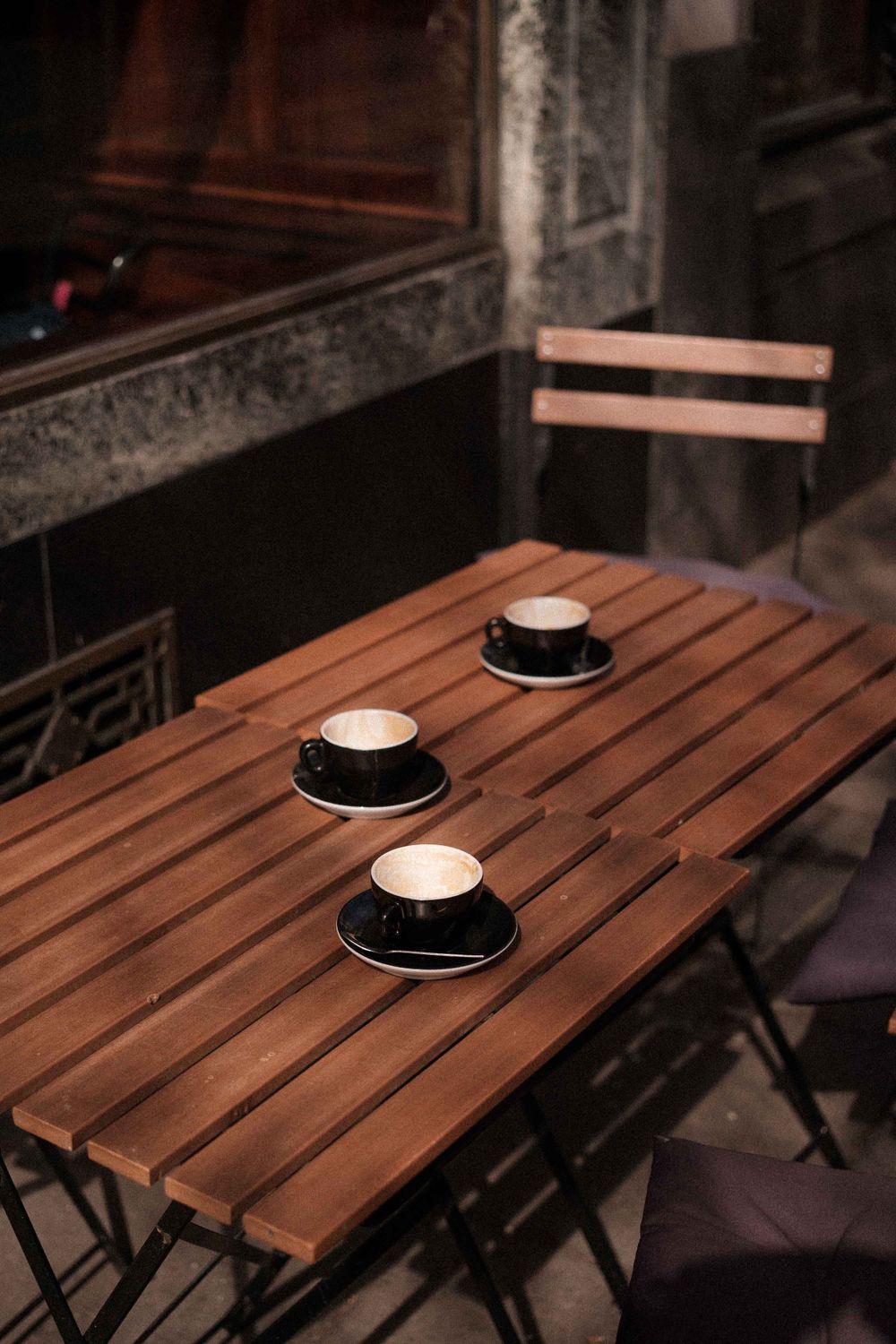 Three white coffee cups on black saucers arranged on a wooden outdoor table.