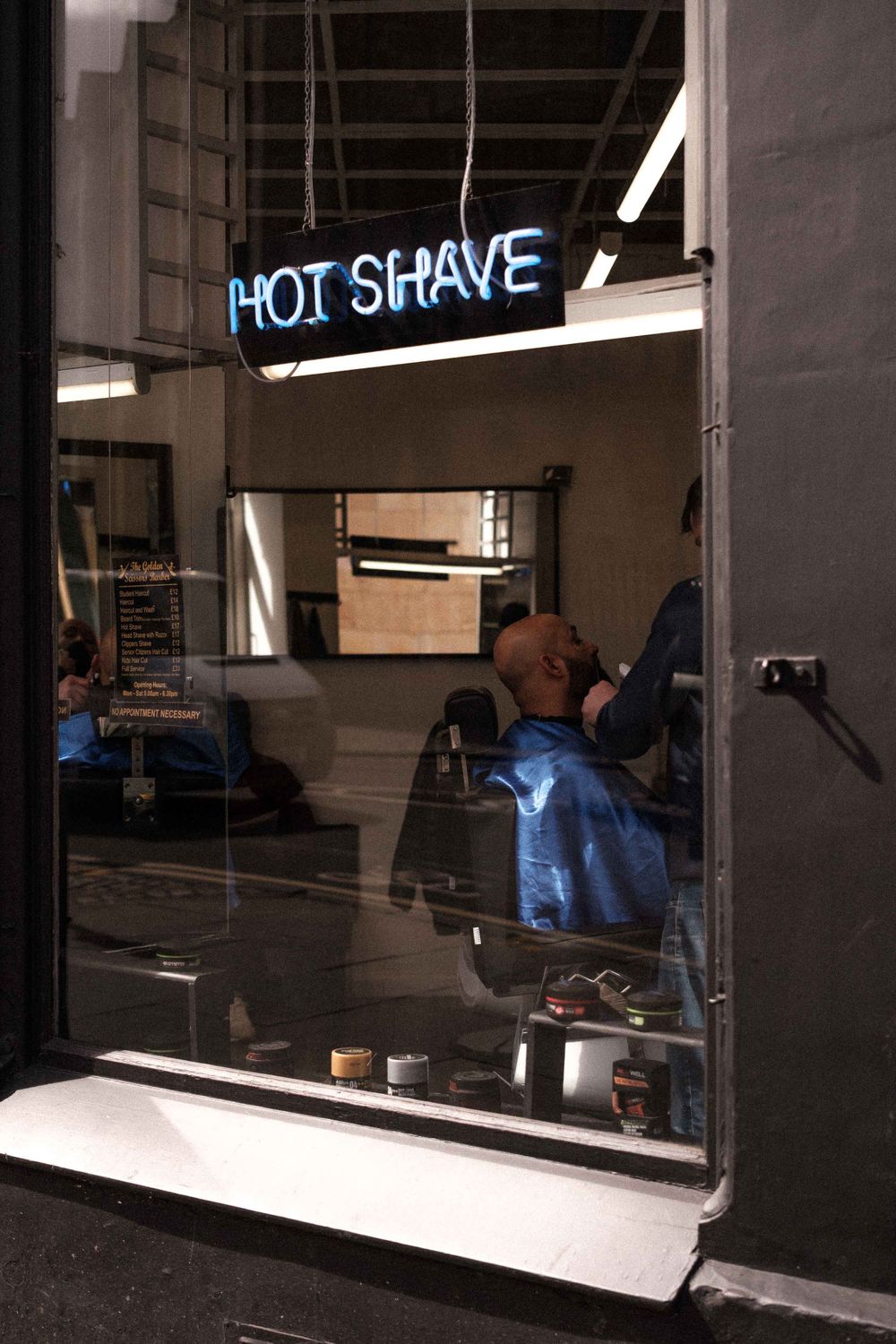 Blue neon 'Hot Shave' sign glowing in a barber shop window.